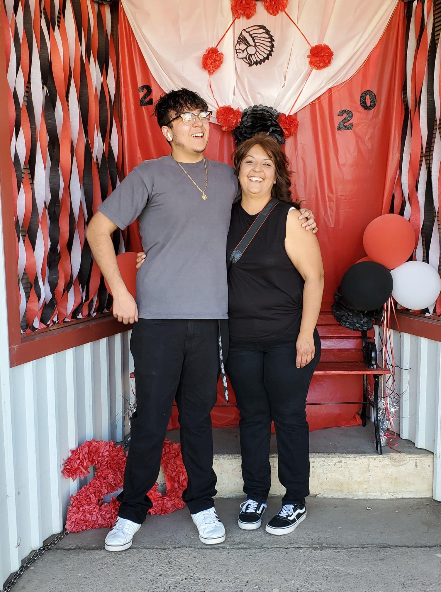 Anna and son Angel Villalobos in front of outdoor Cricut graduation photo booth for Cobre High School