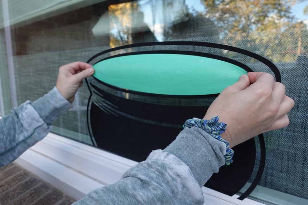 hand-placing a vinyl decal for a Halloween window silhouette scene
