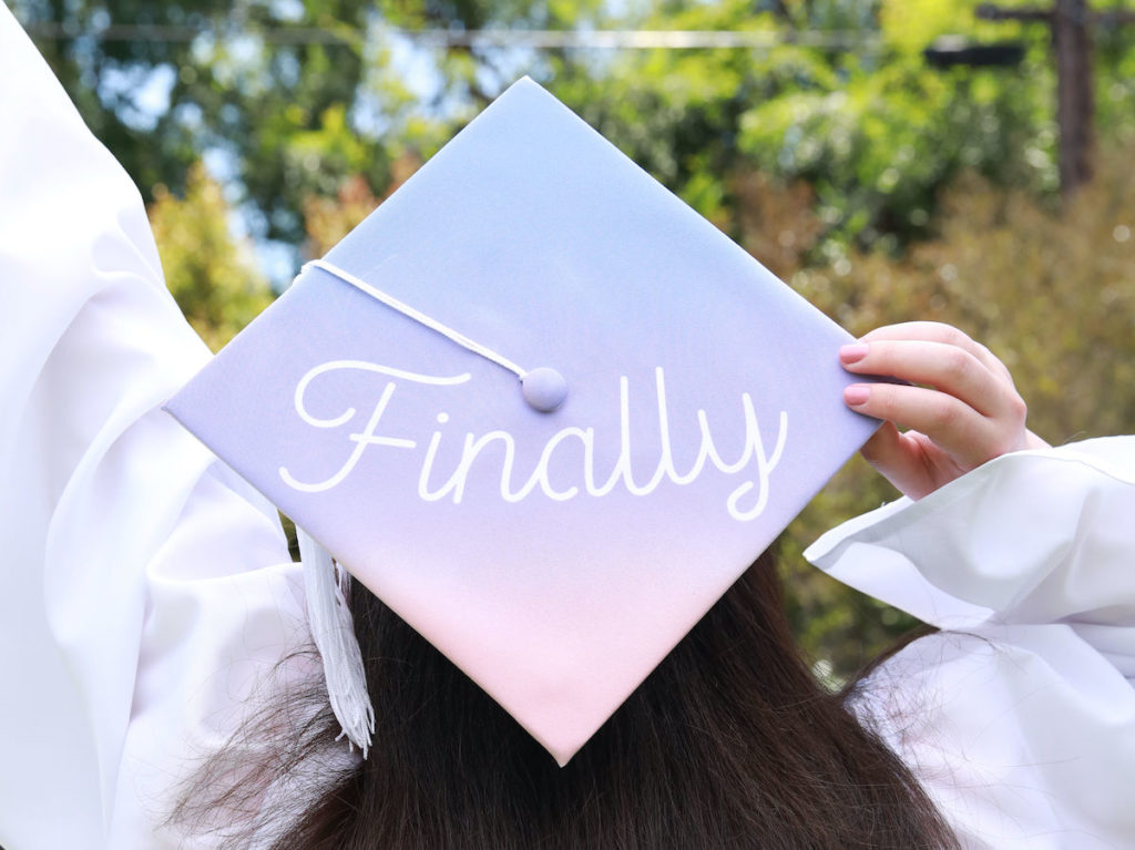 A gradient purple and pink grad cap sits atop a student's head. The graduation cap design reads "Finally" in white font on top.