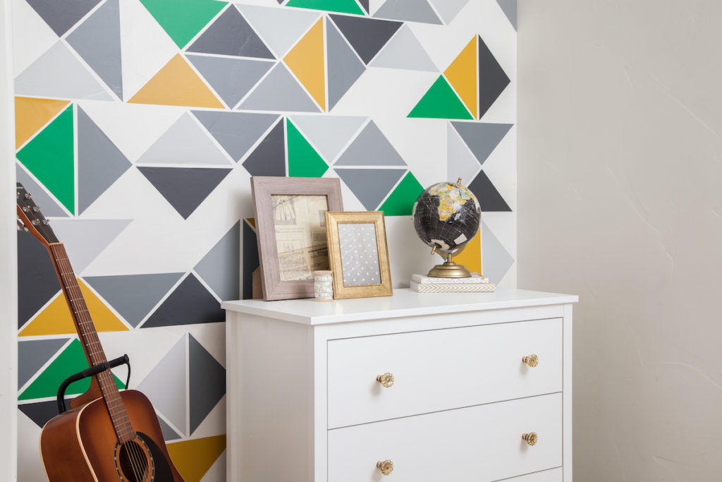 A geometric wall design sits behind a white bookshelf