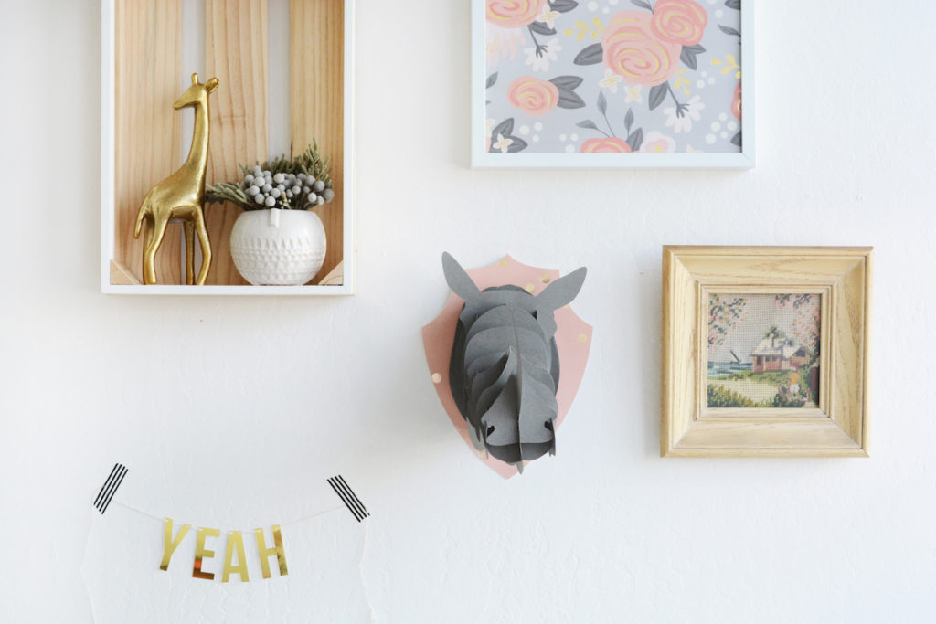 Interesting art and photo frames sit along a wall, with a banner that reads "yeah" and a paper rhinoceros head.