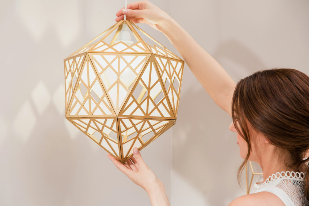 A woman hangs a handmade, gold lamp from her ceiling.