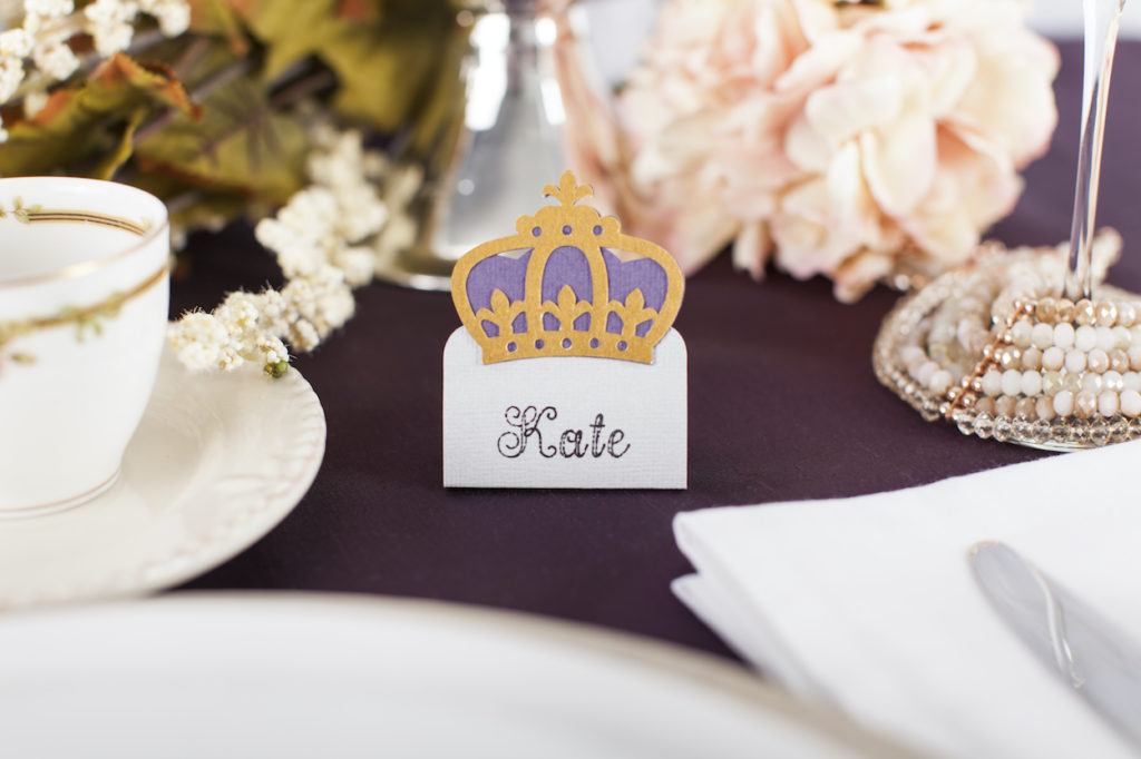A regal looking name tag sits next to a ceramic place setting. 