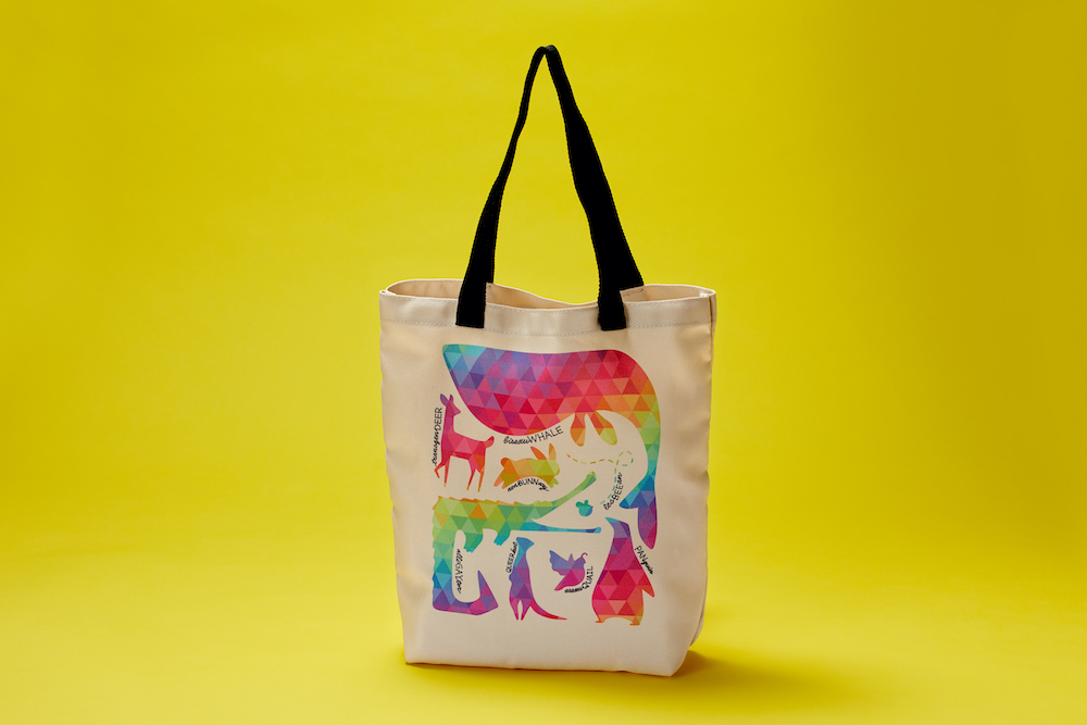 A colorful pattern of animal silhouettes is printed on a tan tote bag