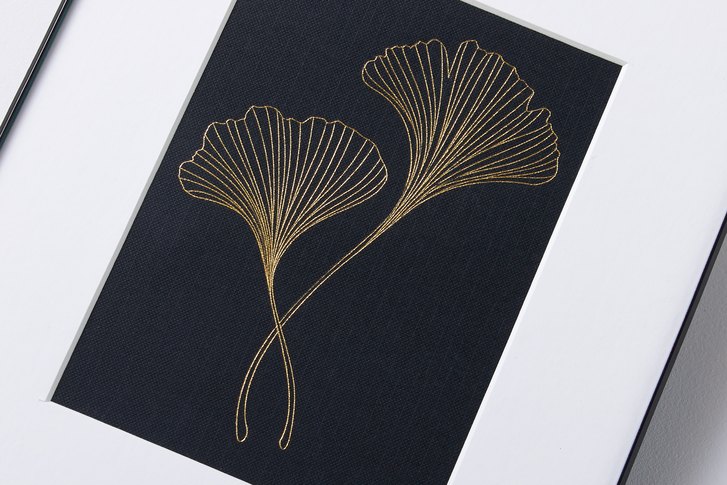 Golden line art of a gincko flower is impressed upon a black canvas