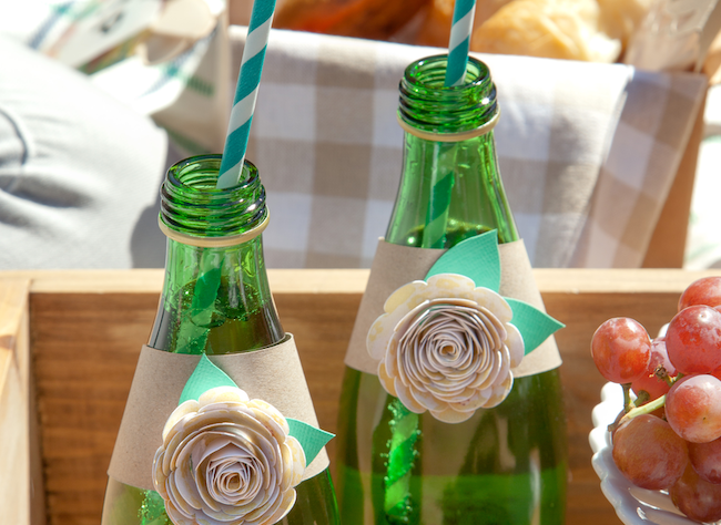 Green glass water bottles are wrapped with paper flower embellishments