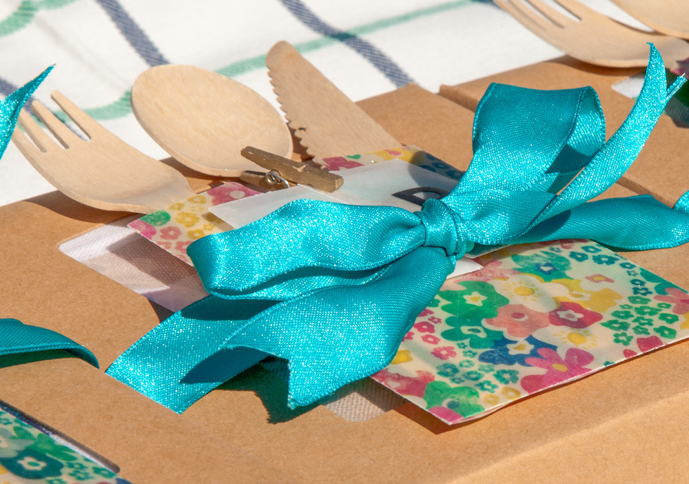 Wooden cutlery is nestled inside a floral paper sleeve, topped with a blue bow
