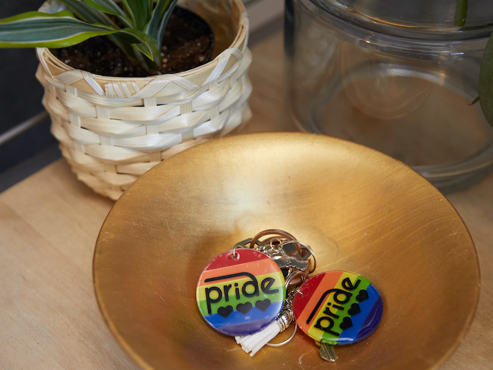 Two rainbow colored pride keychains sit in a gold catch-all dish. 
