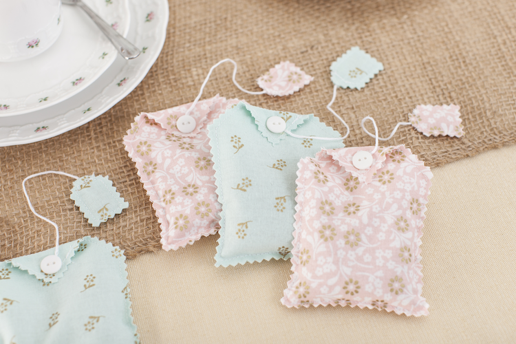 Fabric tea bag sachets in pink and blue sit on a brown table