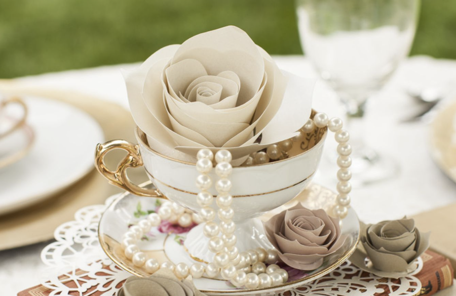A white tea cup is surrounded by neutral colored paper roses and pearls