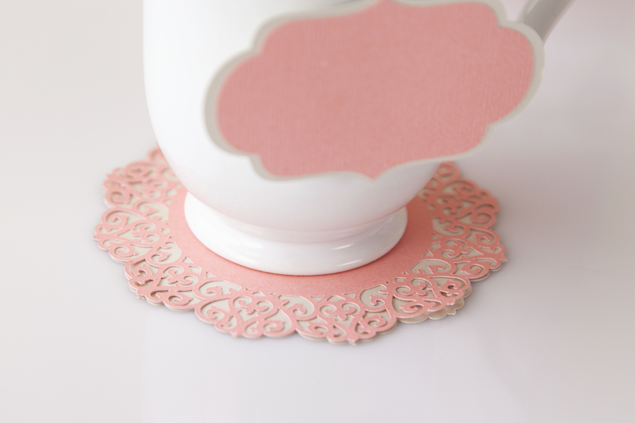 A white teacup sits on a pink lacey paper design