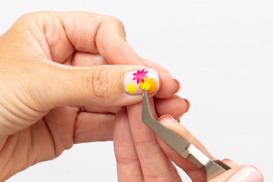 A woman uses a pair of tweezers to apply vinyl to her summer nails design