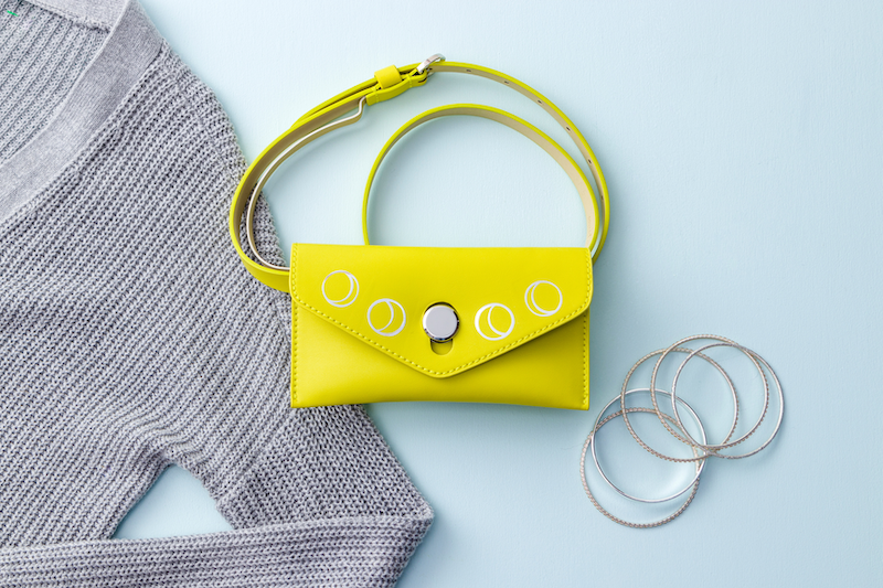 A yellow handbag sits on a blue background next to a grey sweater