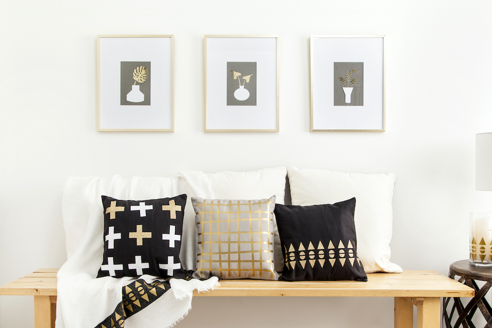A bench is decorated in metallic decor, including decorative pillows and golden wall art prints