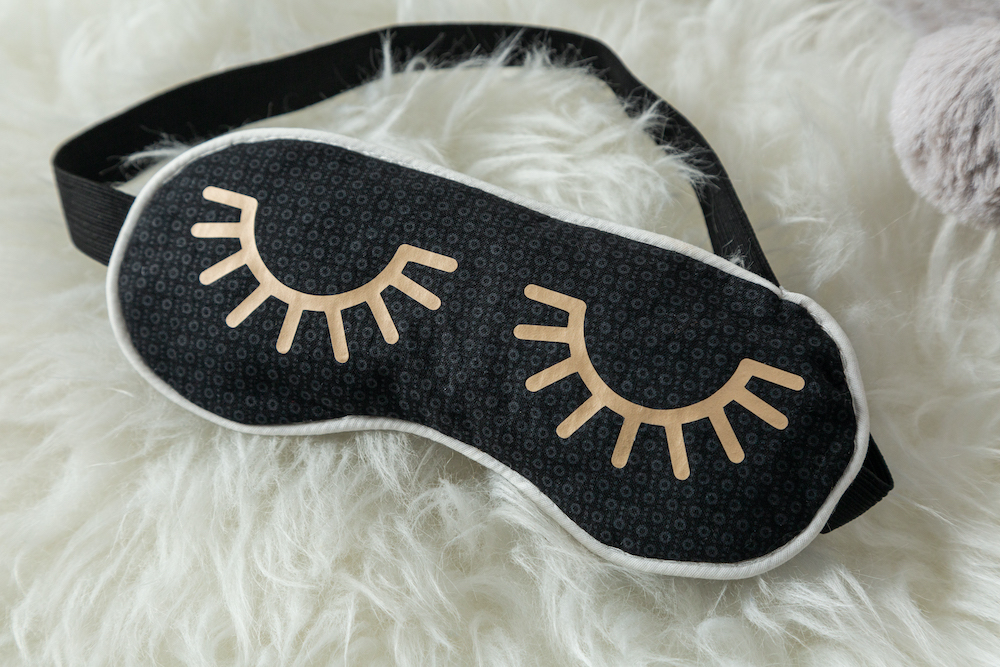 A black sleep mask with golden eyelashes ironed on the front 