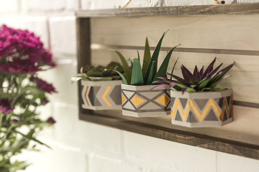 Paper plants sit inside a wooden and gold foil planter being hung outdoors as metallic decor