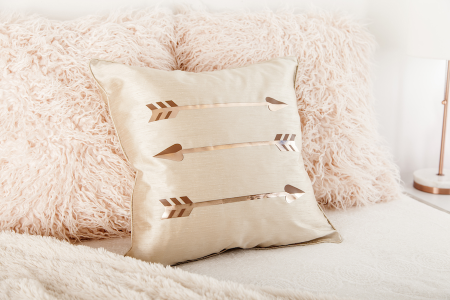 A metallic decor pillow is covered with gold foil printed arrow designs