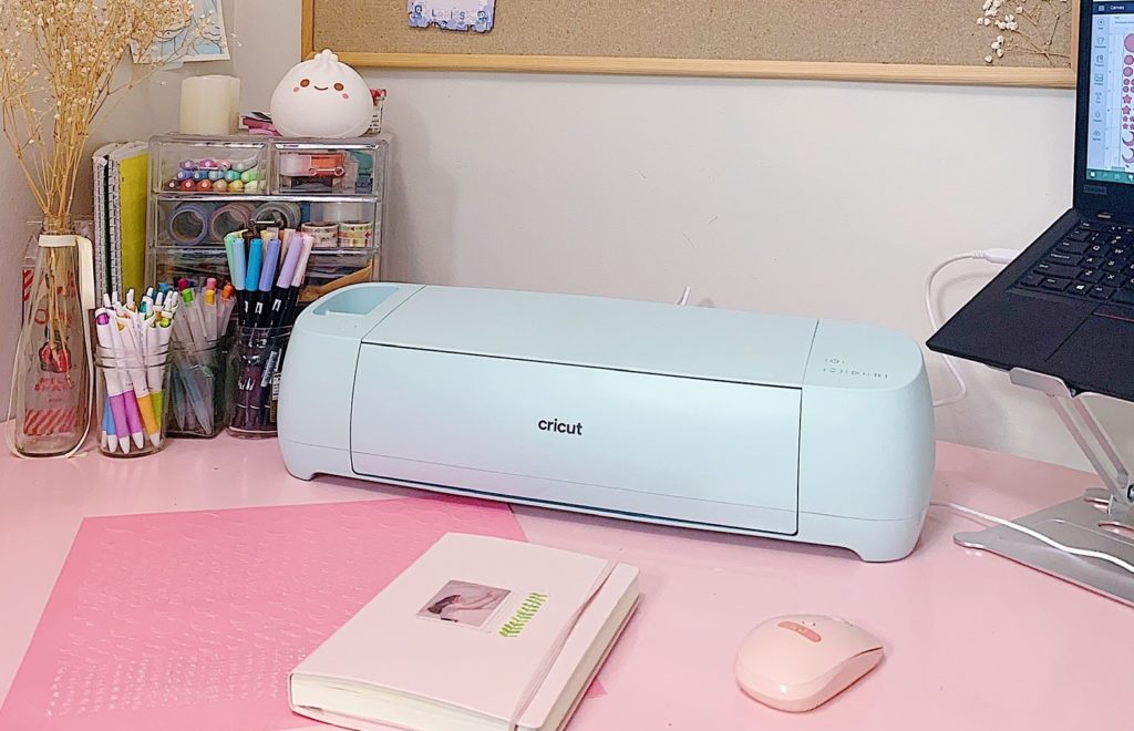 A Cricut Explore 3 machine sits on a pink desk, awaiting cut instructions to create bullet journaling stickers