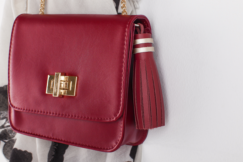 A wine colored handbag with a leather tassel is hung on a wall 