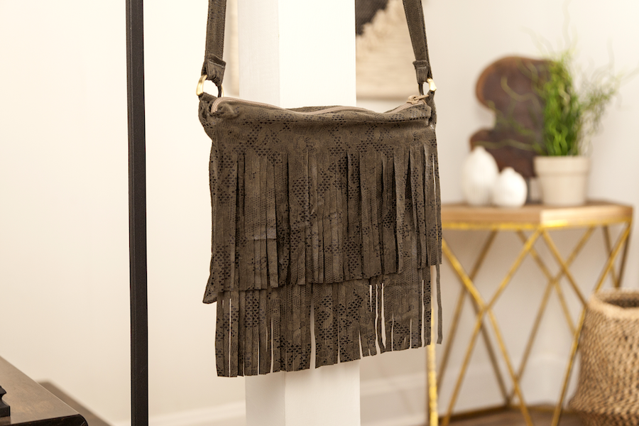 A brown tasseled faux suede handbag hangs from an iron rod