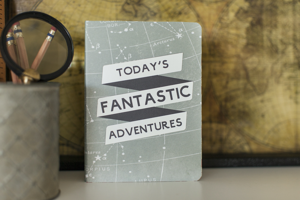 A light blue travel notebook has the phrase "today's fantastic adventures" on the front cover