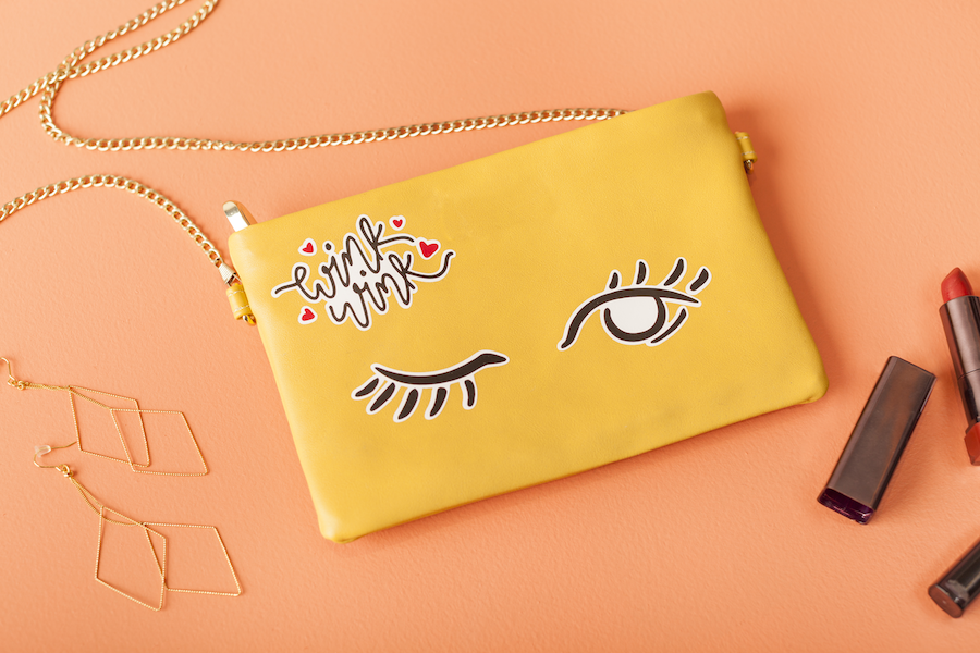 A yellow clutch handbag with a winky face design sits on a peach colored background