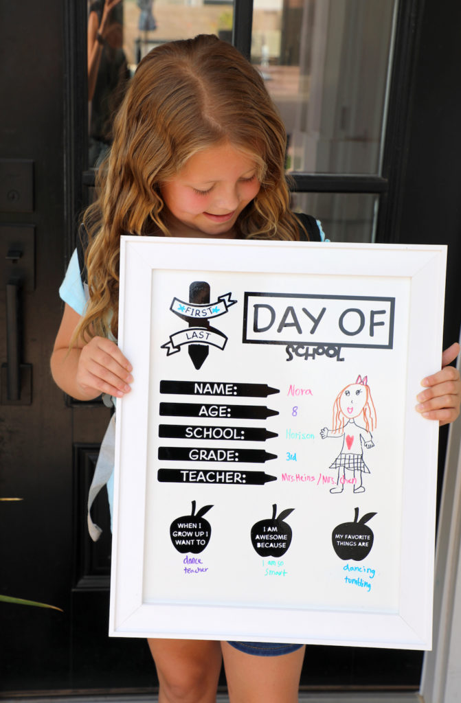 A little girl holds up her drawings and answers written on a back-to-school white board photo shoot prop 