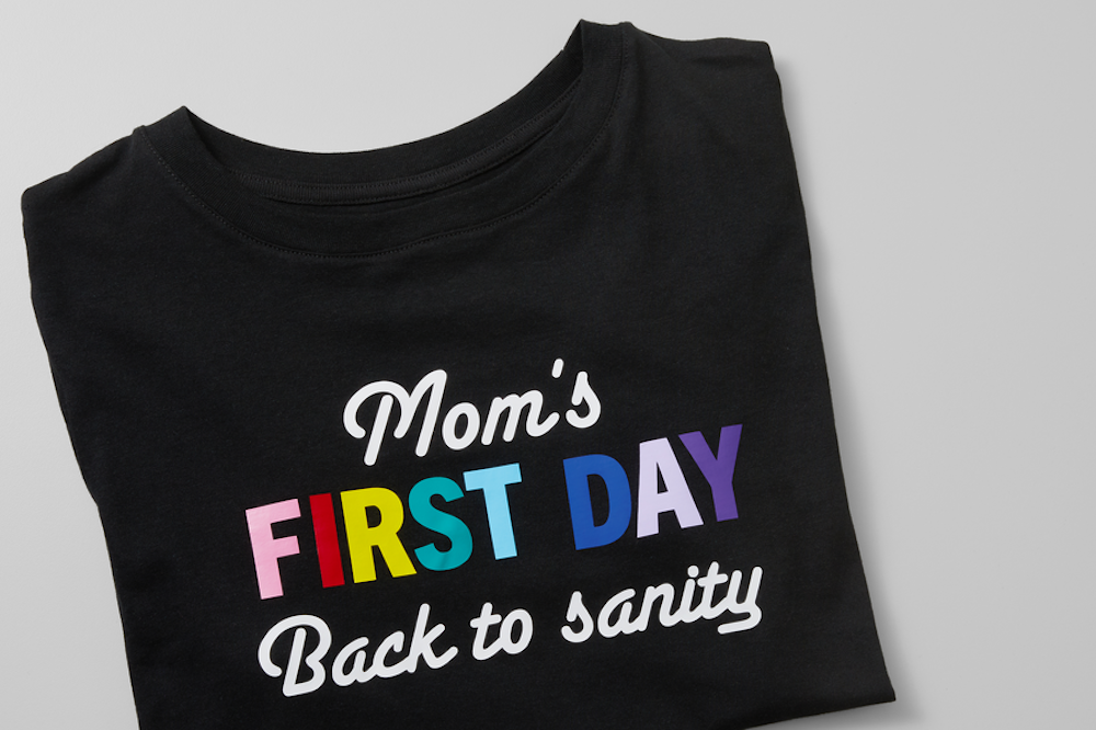 A black back-to-school t-shirt for moms reading "mom's first day back to sanity" sits on a grey surface 