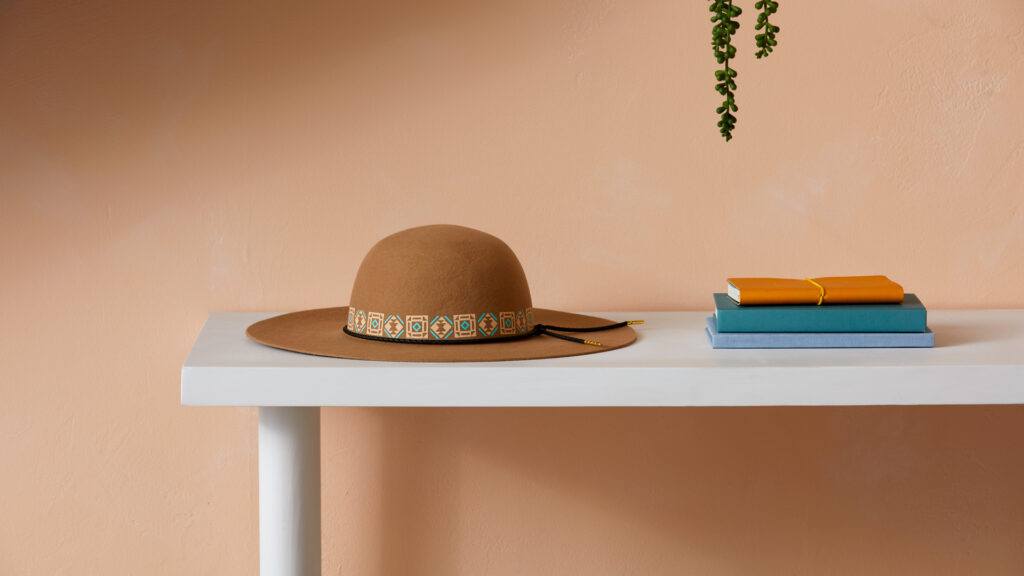 customized sun hat sitting on white table with blue and orange book against a peach wall