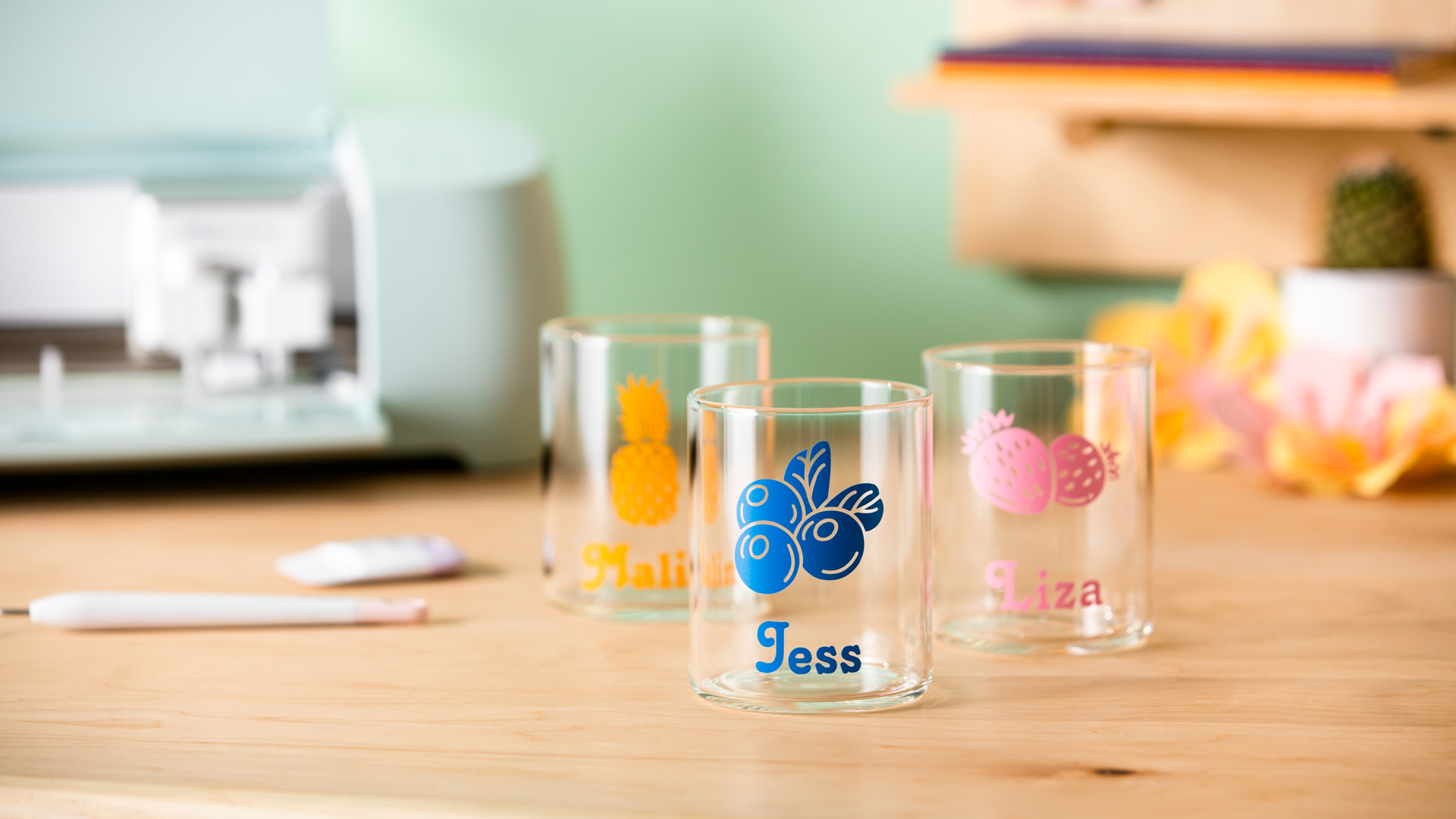 Finished personalized glassware sitting on wood table with Cricut cutting machine in background